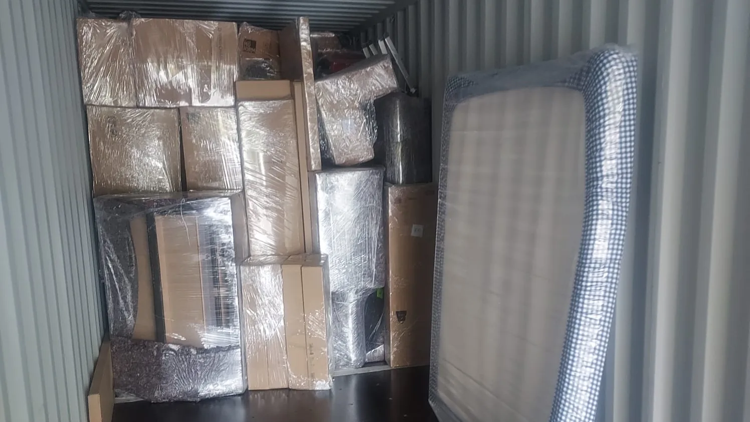 Furniture, a mattress and boxes wrapped in plastic film and loaded inside a shipping container